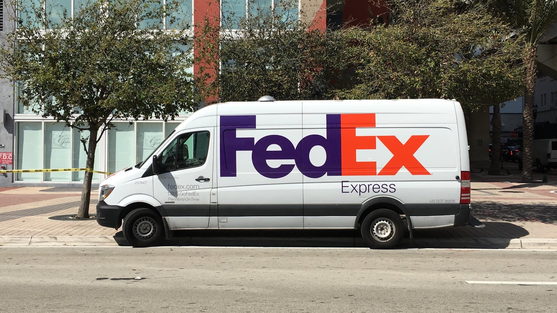 A white FedEx Express van parked at the curb on a downtown Miami street.